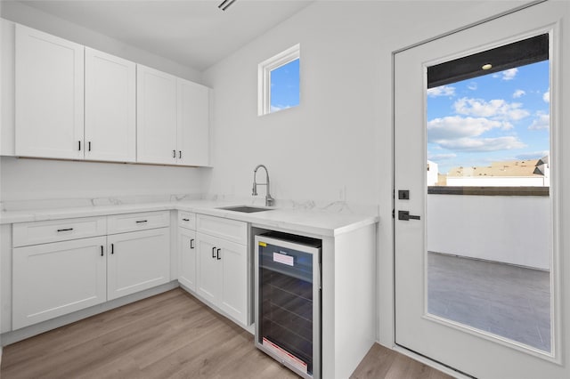 kitchen with light wood-style floors, beverage cooler, white cabinets, and a sink