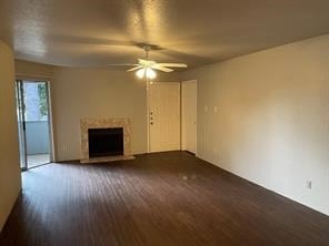 unfurnished living room with a fireplace with raised hearth, ceiling fan, and wood finished floors