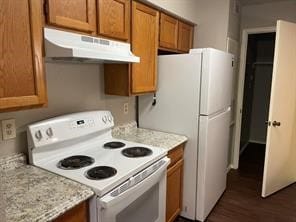 kitchen featuring white appliances, under cabinet range hood, brown cabinetry, and dark wood-type flooring