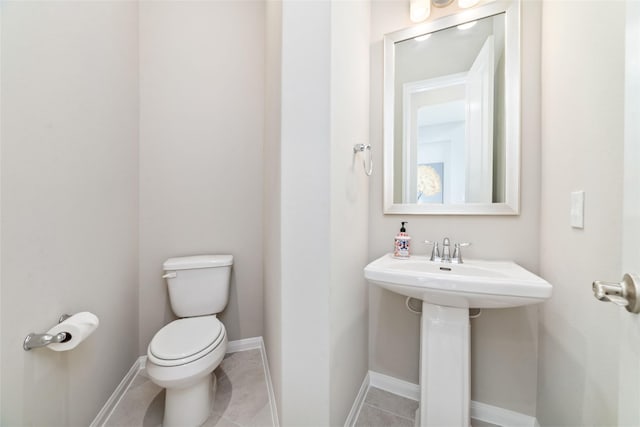 half bath with a sink, tile patterned flooring, toilet, and baseboards