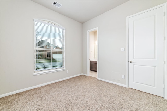 unfurnished bedroom with light carpet, visible vents, baseboards, and ensuite bathroom