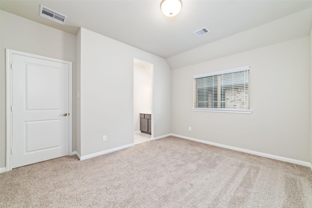 unfurnished bedroom with light colored carpet, visible vents, vaulted ceiling, and baseboards