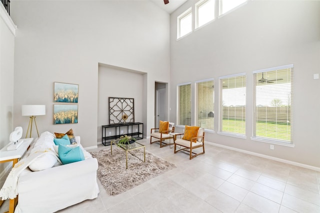 living room featuring light tile patterned floors, a high ceiling, a ceiling fan, and baseboards