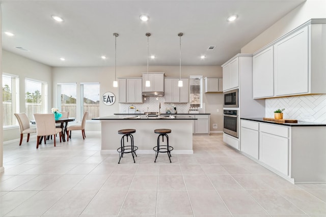 kitchen featuring oven, under cabinet range hood, visible vents, built in microwave, and dark countertops