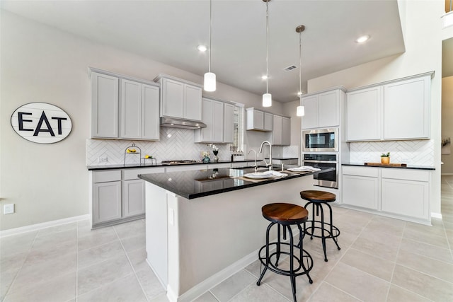 kitchen with under cabinet range hood, a sink, visible vents, appliances with stainless steel finishes, and dark countertops