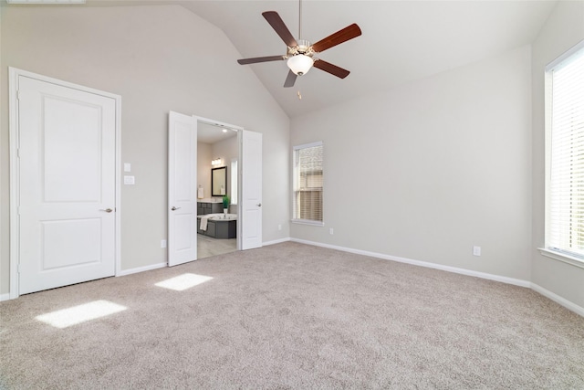 unfurnished bedroom with ceiling fan, high vaulted ceiling, connected bathroom, light colored carpet, and baseboards