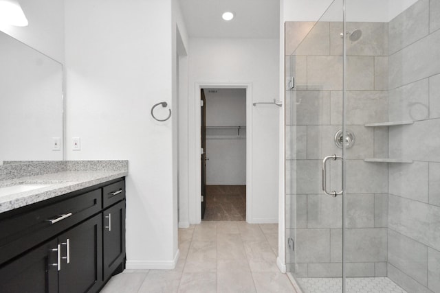 full bath featuring vanity, a shower stall, a spacious closet, and baseboards