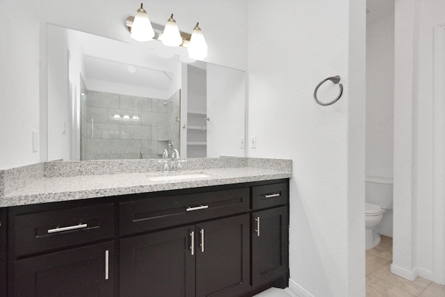 bathroom with vanity, baseboards, tiled shower, tile patterned flooring, and toilet