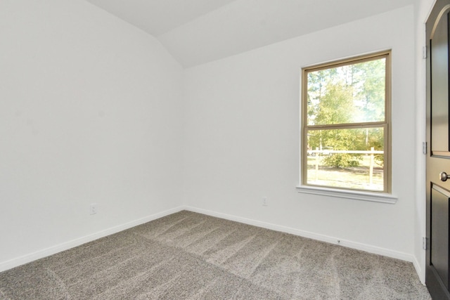 carpeted empty room featuring baseboards and vaulted ceiling