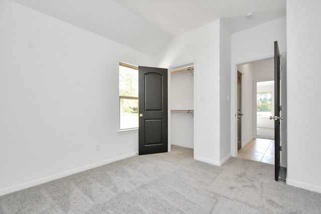 unfurnished bedroom with light tile patterned floors, light colored carpet, baseboards, and lofted ceiling