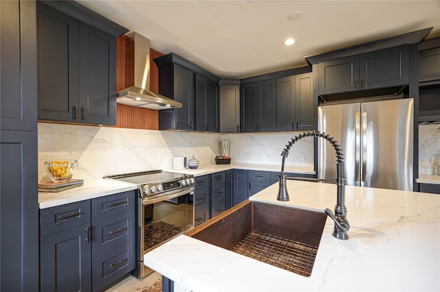 kitchen with stainless steel appliances, a sink, wall chimney range hood, light stone countertops, and tasteful backsplash