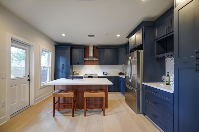 kitchen with visible vents, light countertops, appliances with stainless steel finishes, wall chimney range hood, and tasteful backsplash