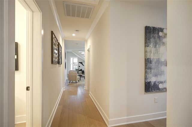 hall featuring crown molding, light wood-type flooring, visible vents, and baseboards