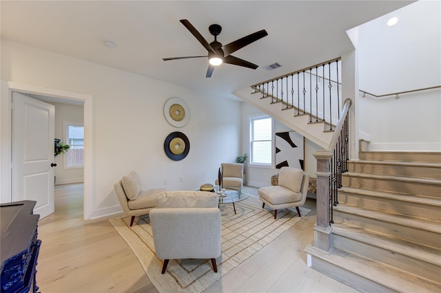 living room with stairway, a ceiling fan, visible vents, and light wood-style floors