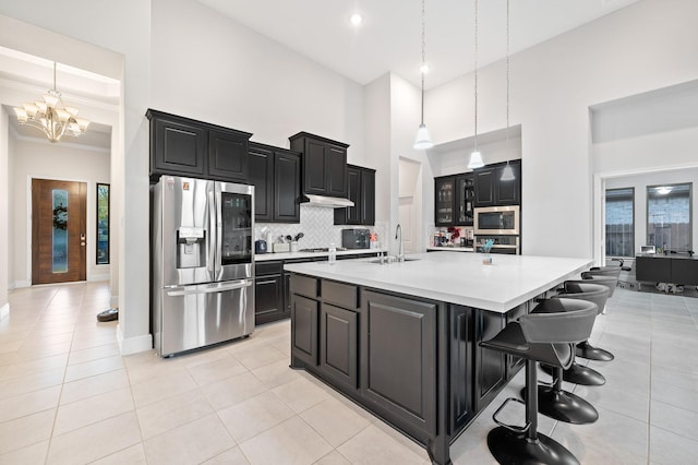 kitchen with dark cabinets, stainless steel appliances, a high ceiling, light countertops, and backsplash