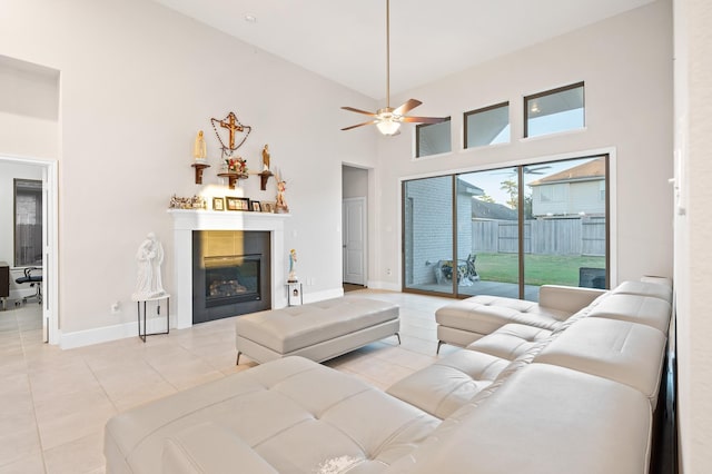 living room featuring light tile patterned floors, baseboards, a ceiling fan, a glass covered fireplace, and a towering ceiling