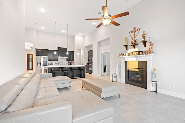 living room with baseboards, a ceiling fan, a tile fireplace, a towering ceiling, and light tile patterned flooring