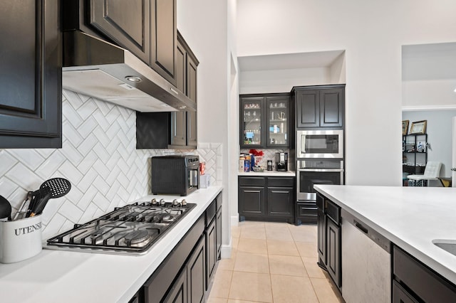 kitchen featuring light tile patterned floors, light countertops, decorative backsplash, appliances with stainless steel finishes, and under cabinet range hood