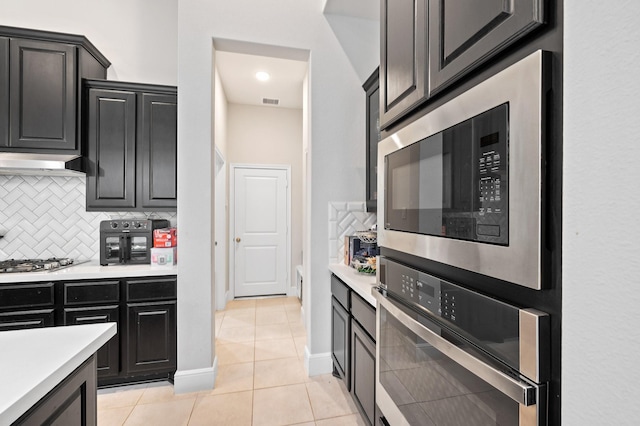 kitchen featuring light tile patterned floors, light countertops, decorative backsplash, appliances with stainless steel finishes, and under cabinet range hood