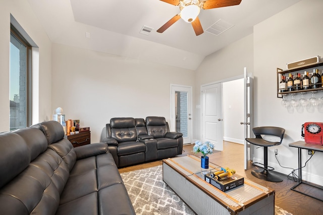 living room featuring lofted ceiling, ceiling fan, visible vents, baseboards, and light wood-style floors