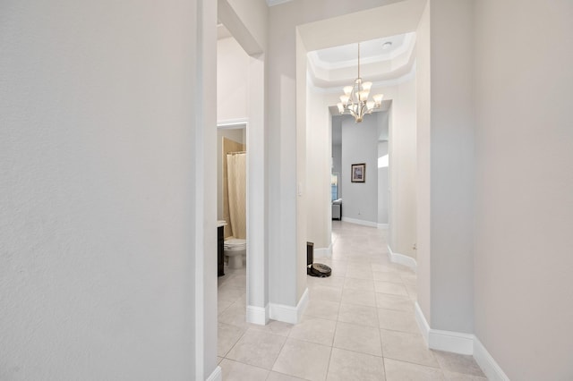 corridor with light tile patterned floors, baseboards, a raised ceiling, an inviting chandelier, and crown molding