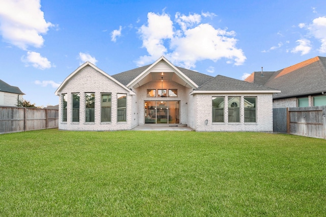 rear view of property with a fenced backyard, roof with shingles, a lawn, and brick siding