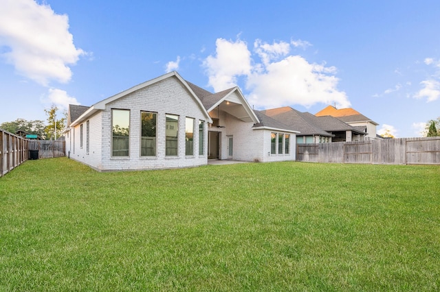 back of house with a fenced backyard, a lawn, and brick siding