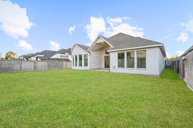 rear view of house with brick siding, a shingled roof, a lawn, a patio area, and a fenced backyard