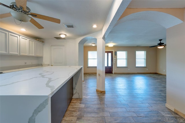 kitchen featuring arched walkways, ceiling fan, light stone counters, visible vents, and open floor plan