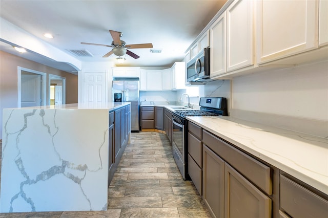 kitchen with ceiling fan, light stone counters, visible vents, white cabinetry, and appliances with stainless steel finishes