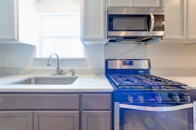 kitchen featuring appliances with stainless steel finishes, backsplash, a sink, and light stone countertops