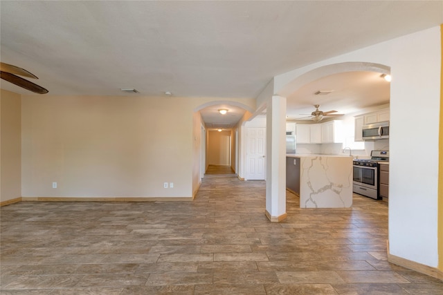 unfurnished living room with arched walkways, a sink, a ceiling fan, and baseboards