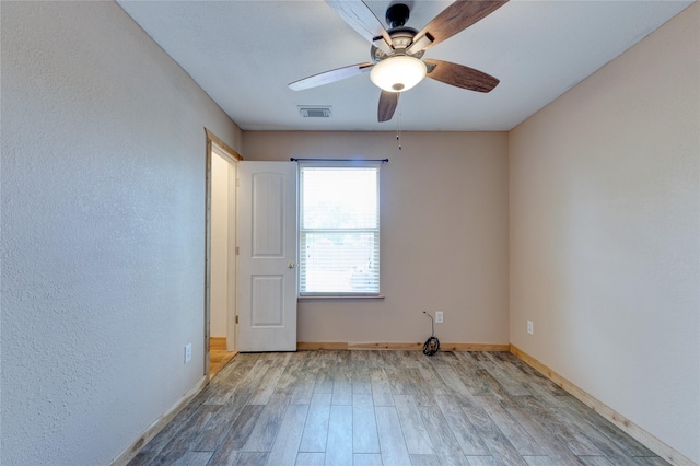 empty room featuring a ceiling fan, visible vents, baseboards, and wood finished floors