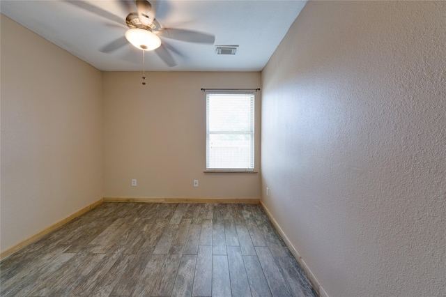 spare room with a ceiling fan, visible vents, baseboards, and wood finished floors