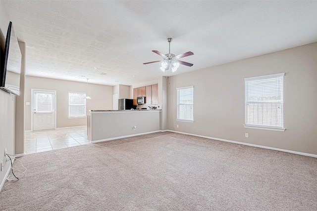 unfurnished living room featuring ceiling fan, a textured ceiling, light tile patterned flooring, light colored carpet, and baseboards