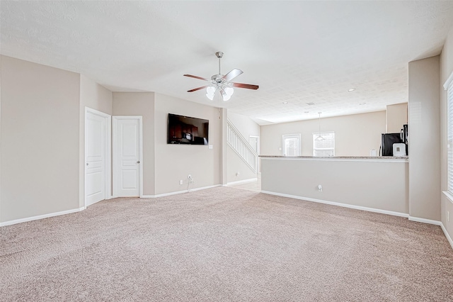 unfurnished living room featuring light colored carpet, ceiling fan, a textured ceiling, and baseboards