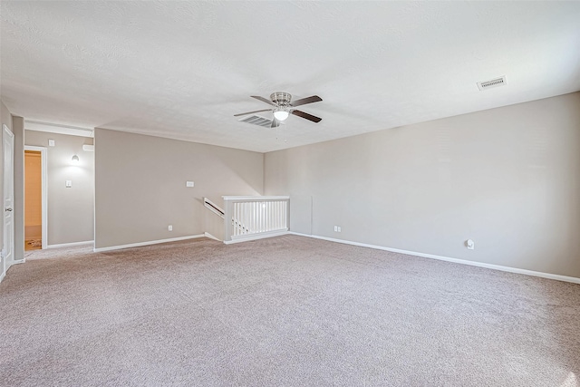 spare room featuring light carpet, baseboards, visible vents, a ceiling fan, and a textured ceiling