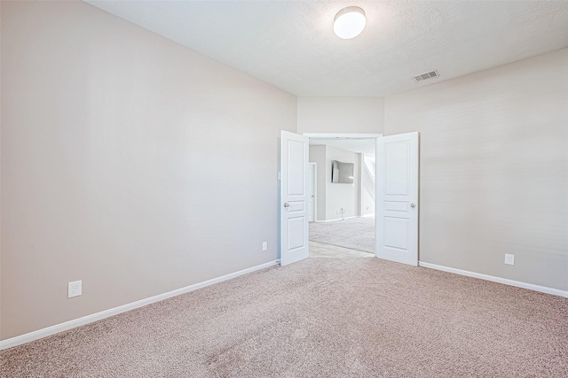 carpeted empty room featuring baseboards, visible vents, and a textured ceiling