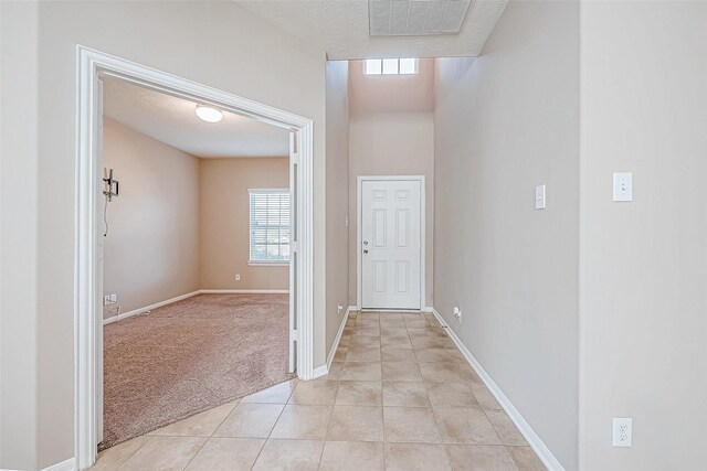 foyer entrance featuring light carpet, a textured ceiling, baseboards, and light tile patterned floors