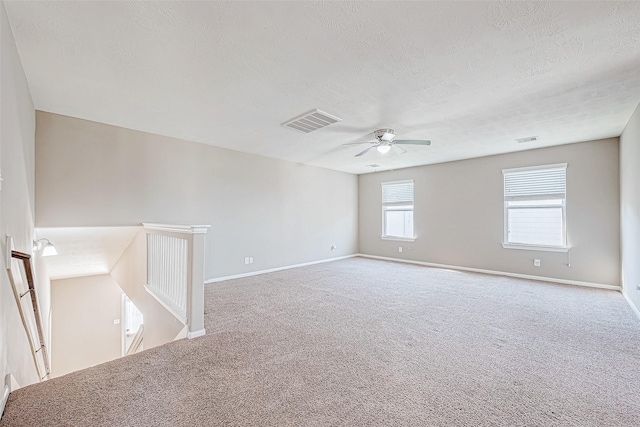 unfurnished room with carpet floors, baseboards, visible vents, and a textured ceiling