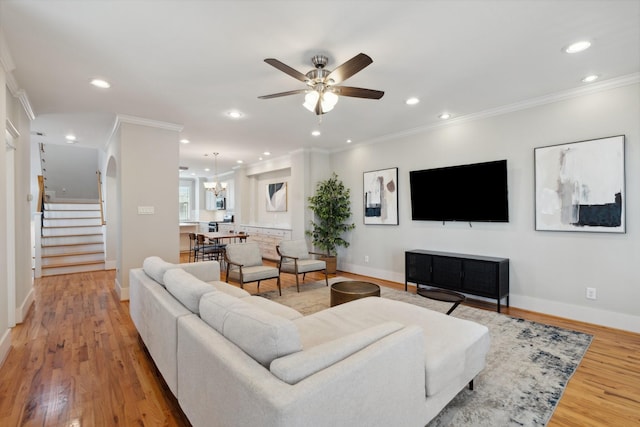 living room with light wood-style flooring, ornamental molding, ceiling fan with notable chandelier, recessed lighting, and stairs