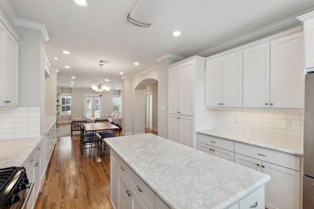 kitchen with arched walkways, wood finished floors, crown molding, and white cabinetry