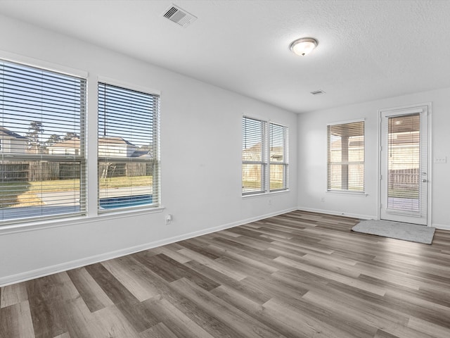 empty room featuring visible vents, a textured ceiling, baseboards, and wood finished floors