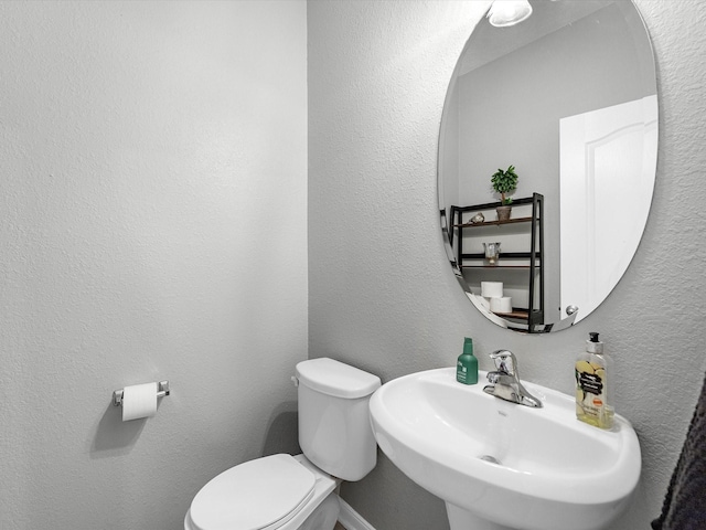 bathroom featuring toilet, a textured wall, and a sink