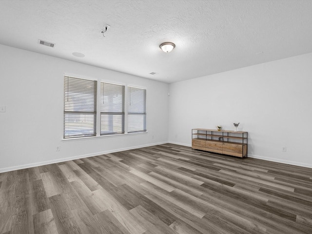 unfurnished room featuring visible vents, baseboards, a textured ceiling, and wood finished floors