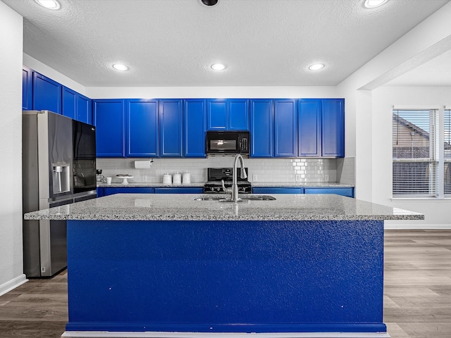 kitchen with blue cabinetry, light stone countertops, wood finished floors, black appliances, and a sink