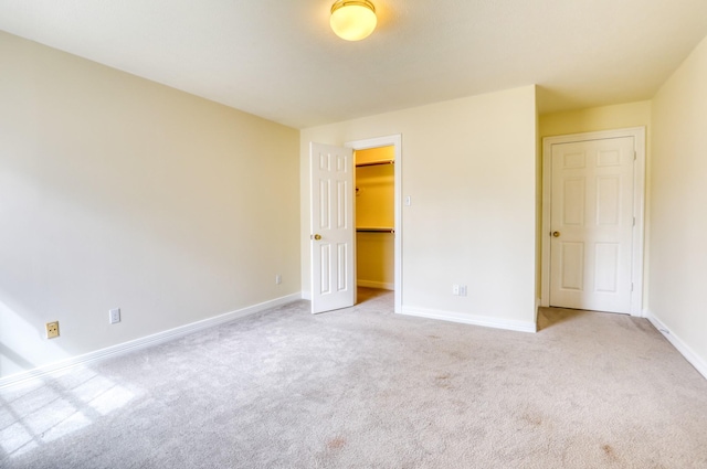 unfurnished bedroom featuring a closet, carpet flooring, a walk in closet, and baseboards