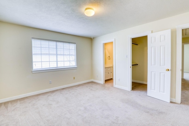 unfurnished bedroom with baseboards, a closet, a textured ceiling, a walk in closet, and light colored carpet