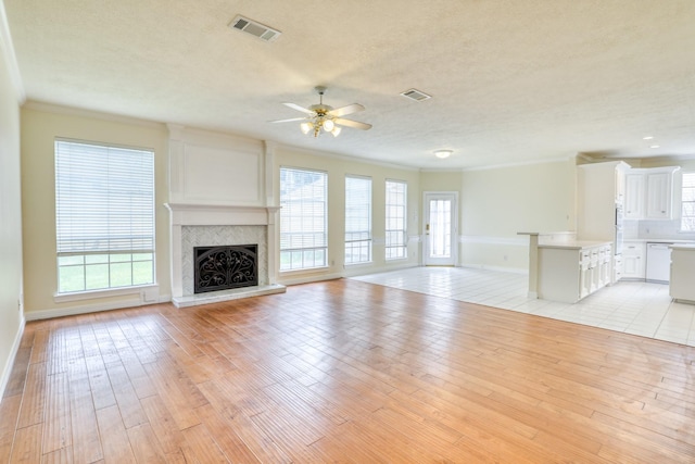 unfurnished living room with light wood-type flooring, visible vents, a fireplace with raised hearth, and crown molding