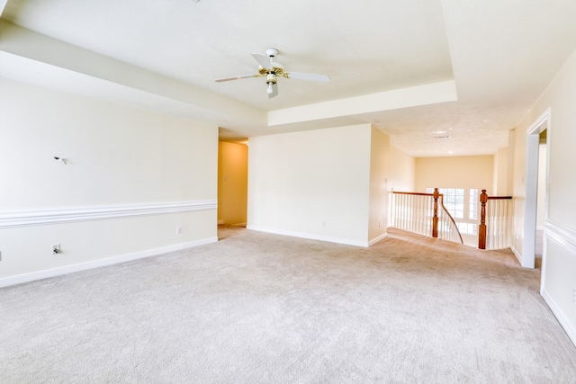 empty room featuring ceiling fan, baseboards, a raised ceiling, and carpet